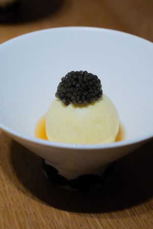 White bowl containing a spherical custard topped with black caviar in sauce.