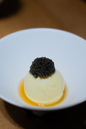 Luxurious dessert featuring black caviar atop cream-colored sphere in white bowl.