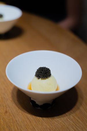 Elegant white bowl containing custard sphere topped with caviar in golden sauce.