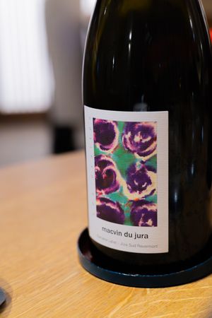 Wine bottle with artistic purple floral label design on wooden table.
