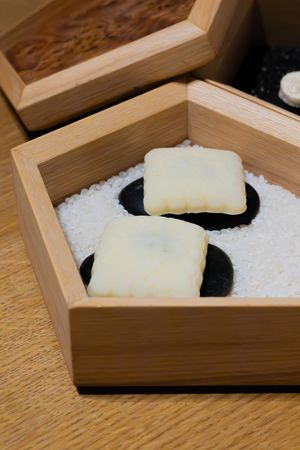 White square treats resting on black plates in a pentagon-shaped wooden box filled with salt.