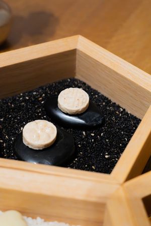 Black stones with beige circular tops displayed on dark granules in a wooden box.