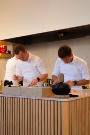 Chefs in white uniforms preparing food at a wooden paneled counter.
