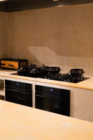 Modern kitchen with black cooktop and built-in ovens against beige wall.