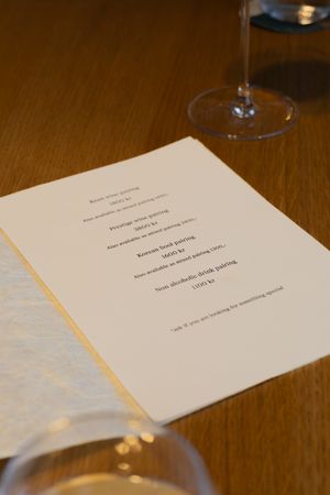 Fine dining menu on white paper with wine glass on wooden table.