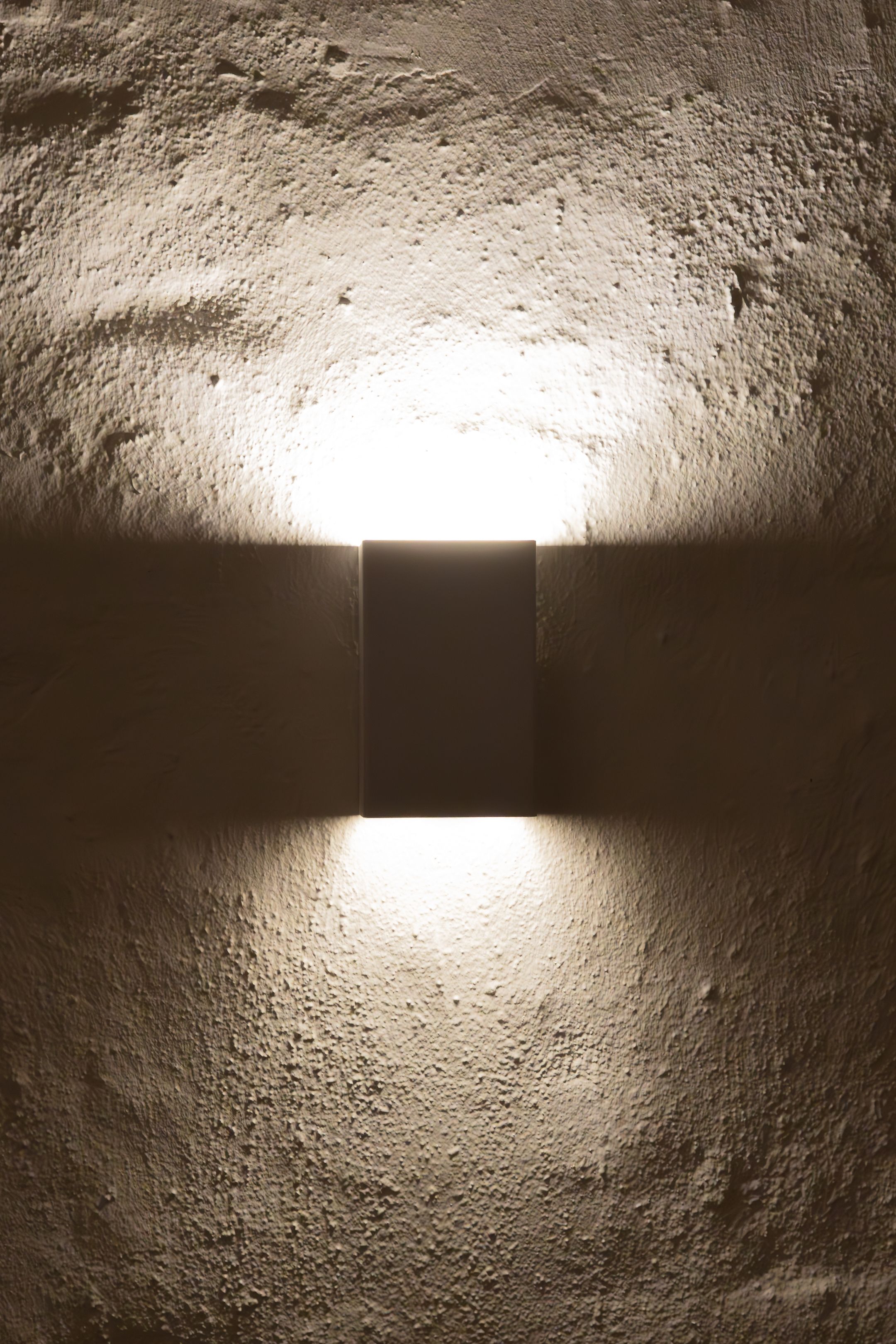 Modern wall sconce creating dramatic textured lighting effect on rough white wall.