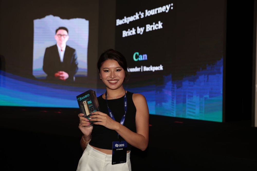 Smiling woman holds Jambo Phone while presenting Backpacks Journey Brick by Brick talk.