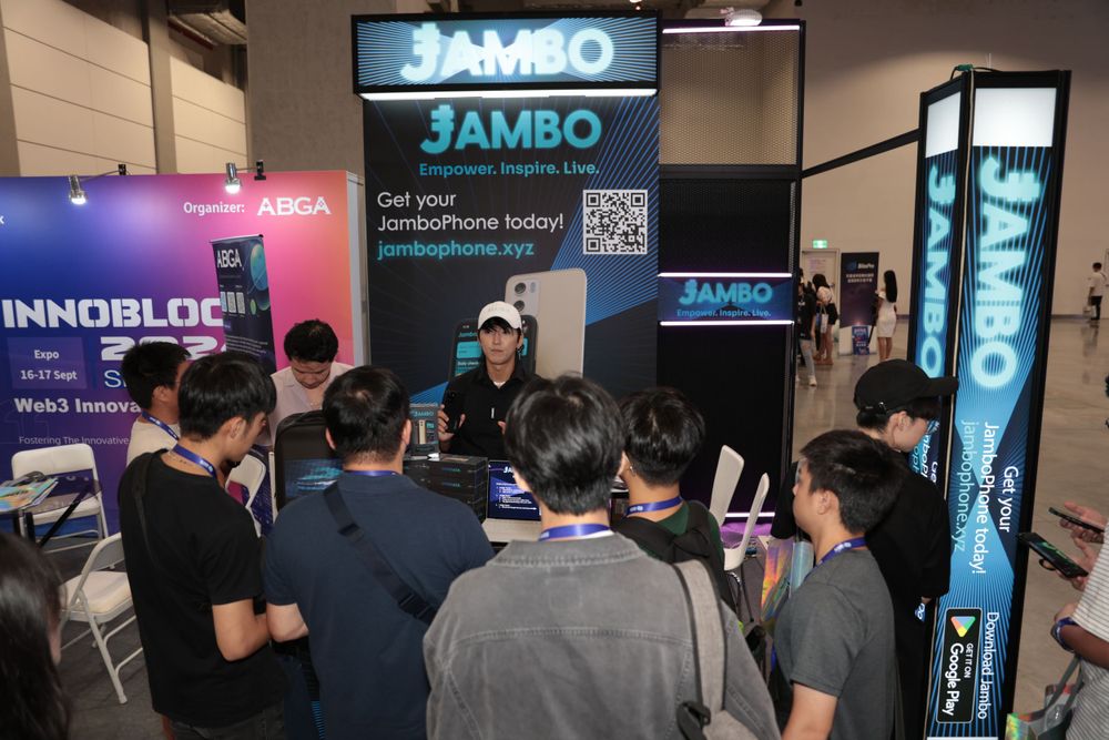 Crowd gathers at Jambo Phone booth display at blockchain technology conference expo floor.