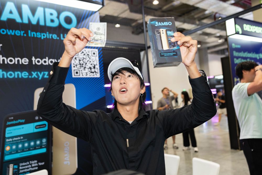 Excited attendee holds up Jambo Phone boxes at a blockchain technology expo booth.