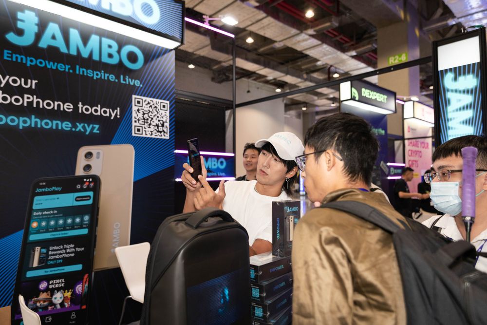 Man examines Jambo smartphone at branded booth during busy tech expo.