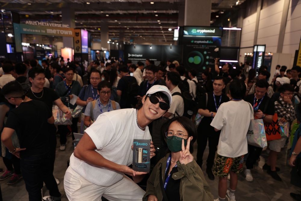 Two people pose together smiling at a crowded technology expo event.