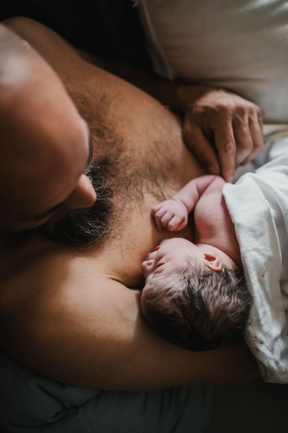 Dad snuggles in bed skin to skin with newborn after this Carson Valley home birth with Ohana Midwifery