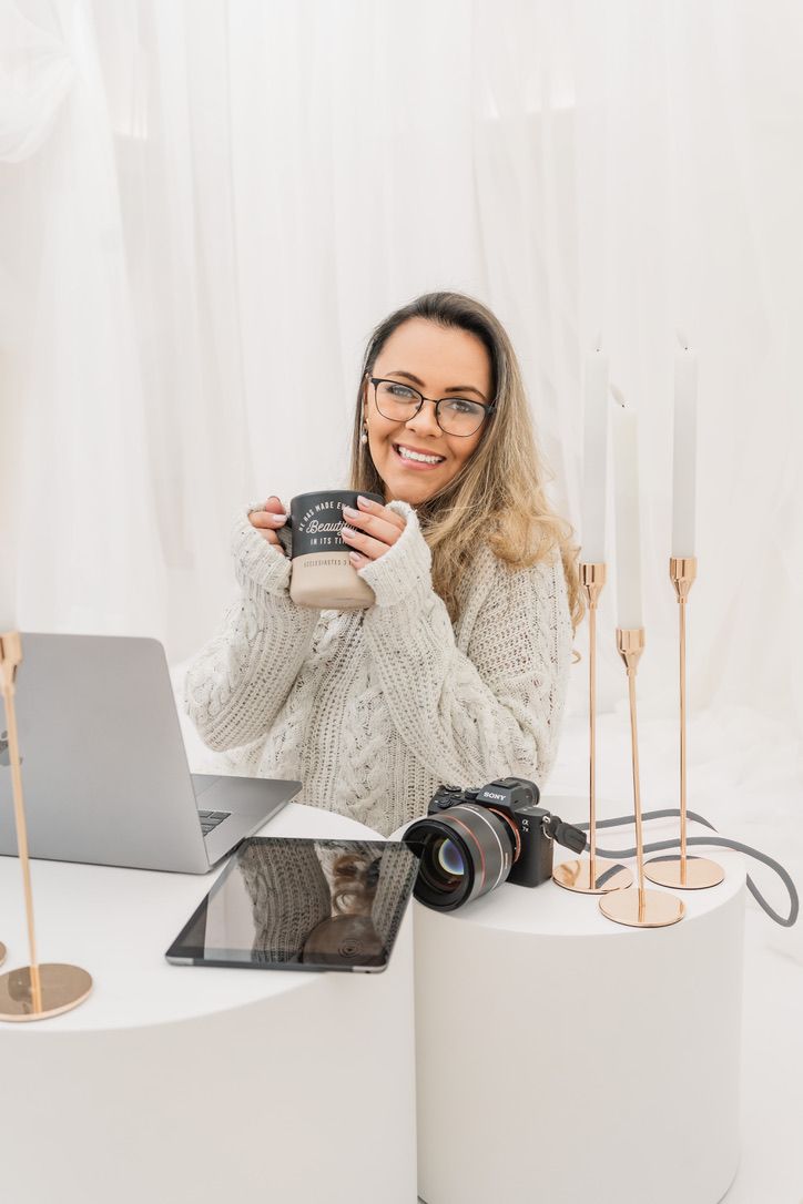 Modern home office setup with laptop, camera, and person enjoying coffee in cozy knit sweater.