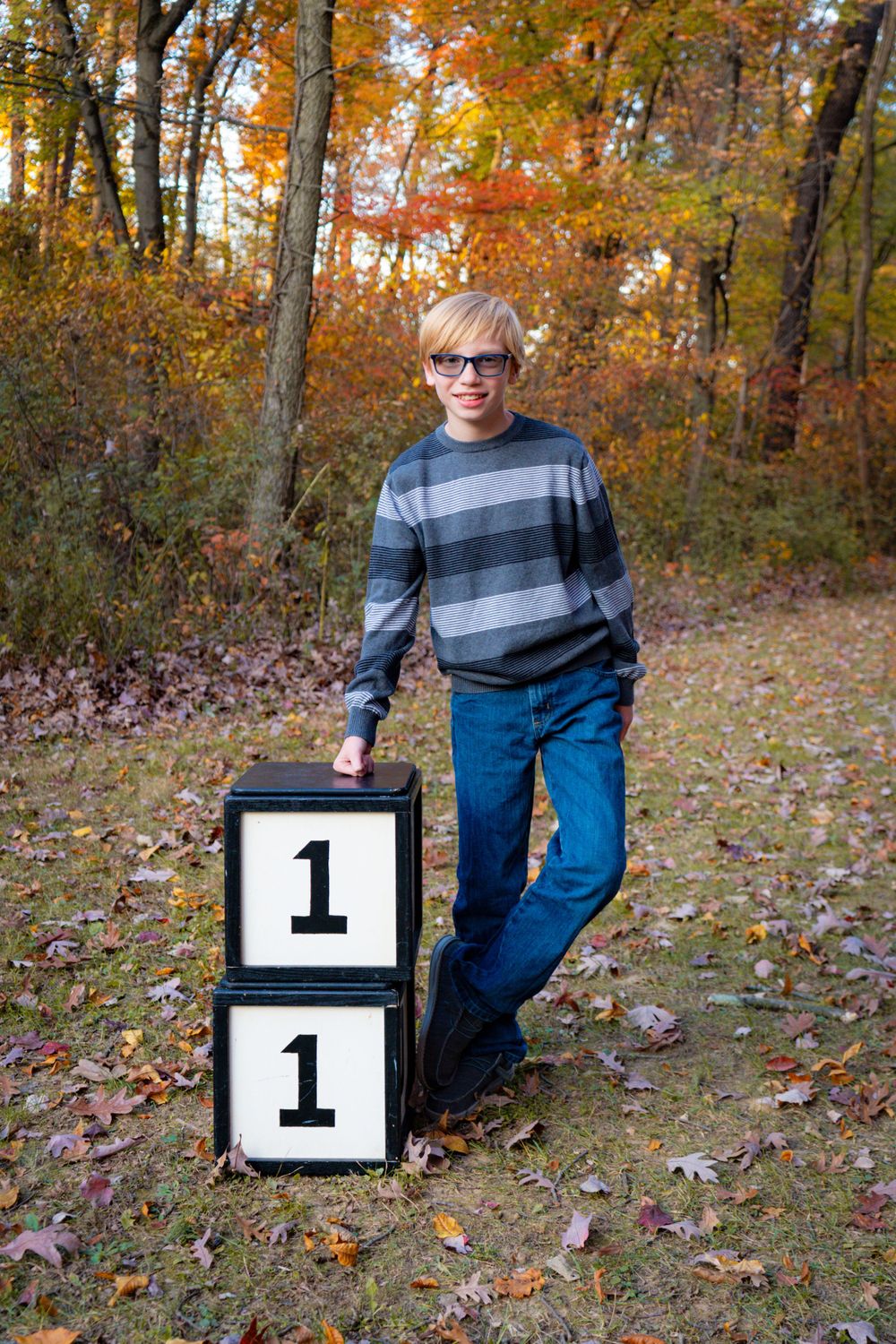 Person in striped sweater leaning against number blocks showing 11 in fall forest setting.