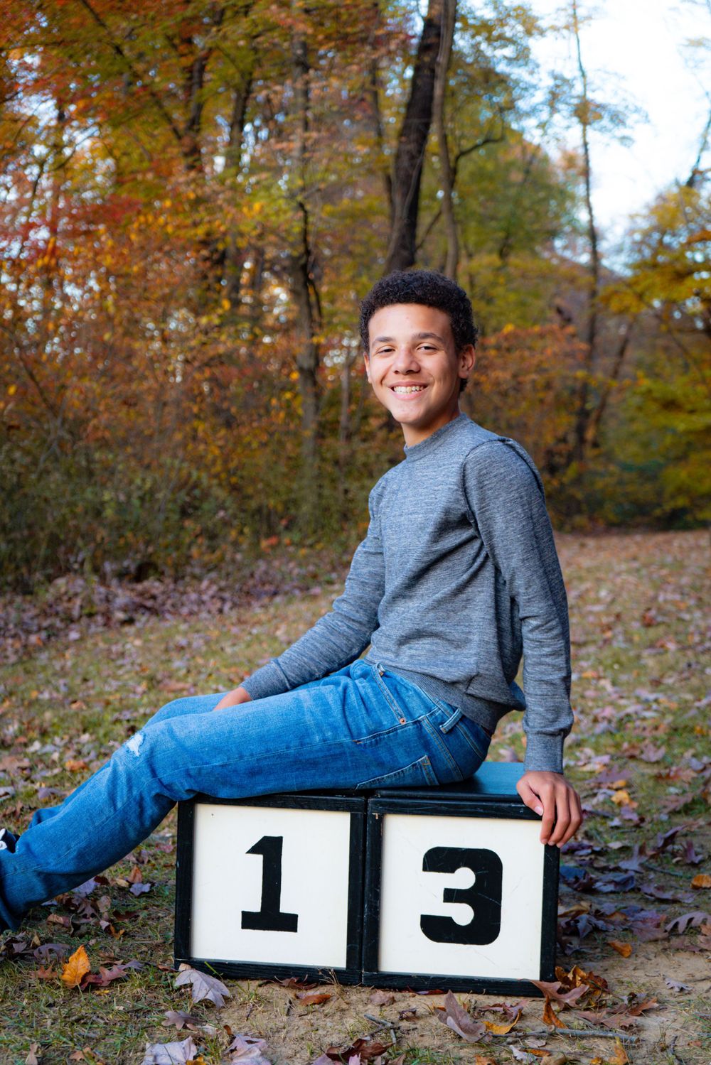 Teen sitting on number blocks displaying 13 during autumn photo session.