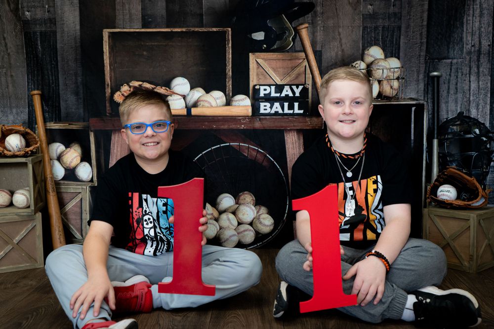 Two youth sitting with sports equipment in storage area wearing matching red and black shirts.