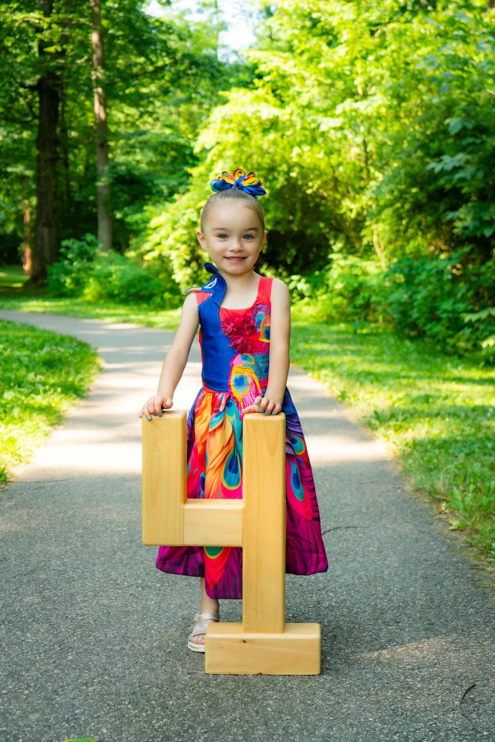 Young child in colorful dress holding large decorative number 4 on outdoor path.