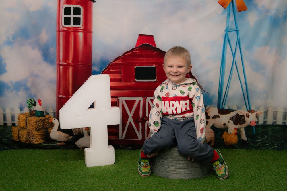 A farm themed fourth birthday photo with red barn backdrop and large white number 4.