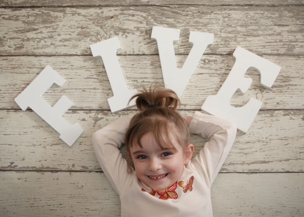 White letters spelling FIVE arranged above a child on weathered wood background.