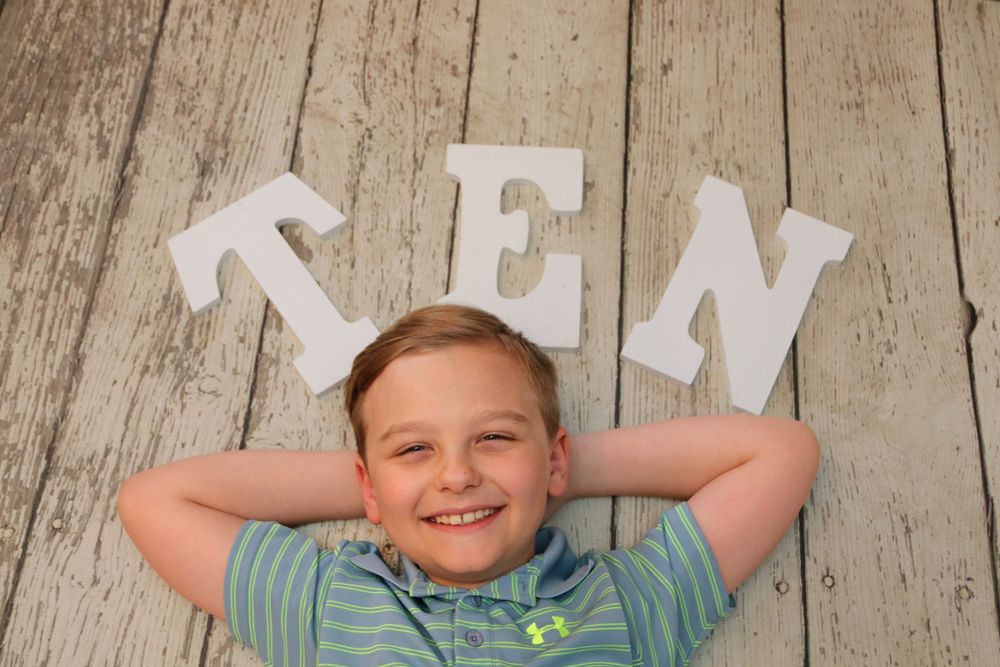 Letters spelling TEN arranged above a reclining child on rustic wooden background.