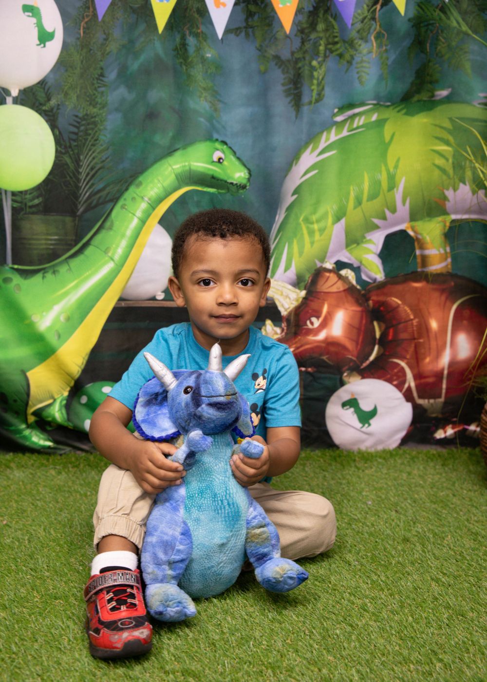 Dinosaur themed party setup with decorative inflatables and colorful banners on artificial grass.
