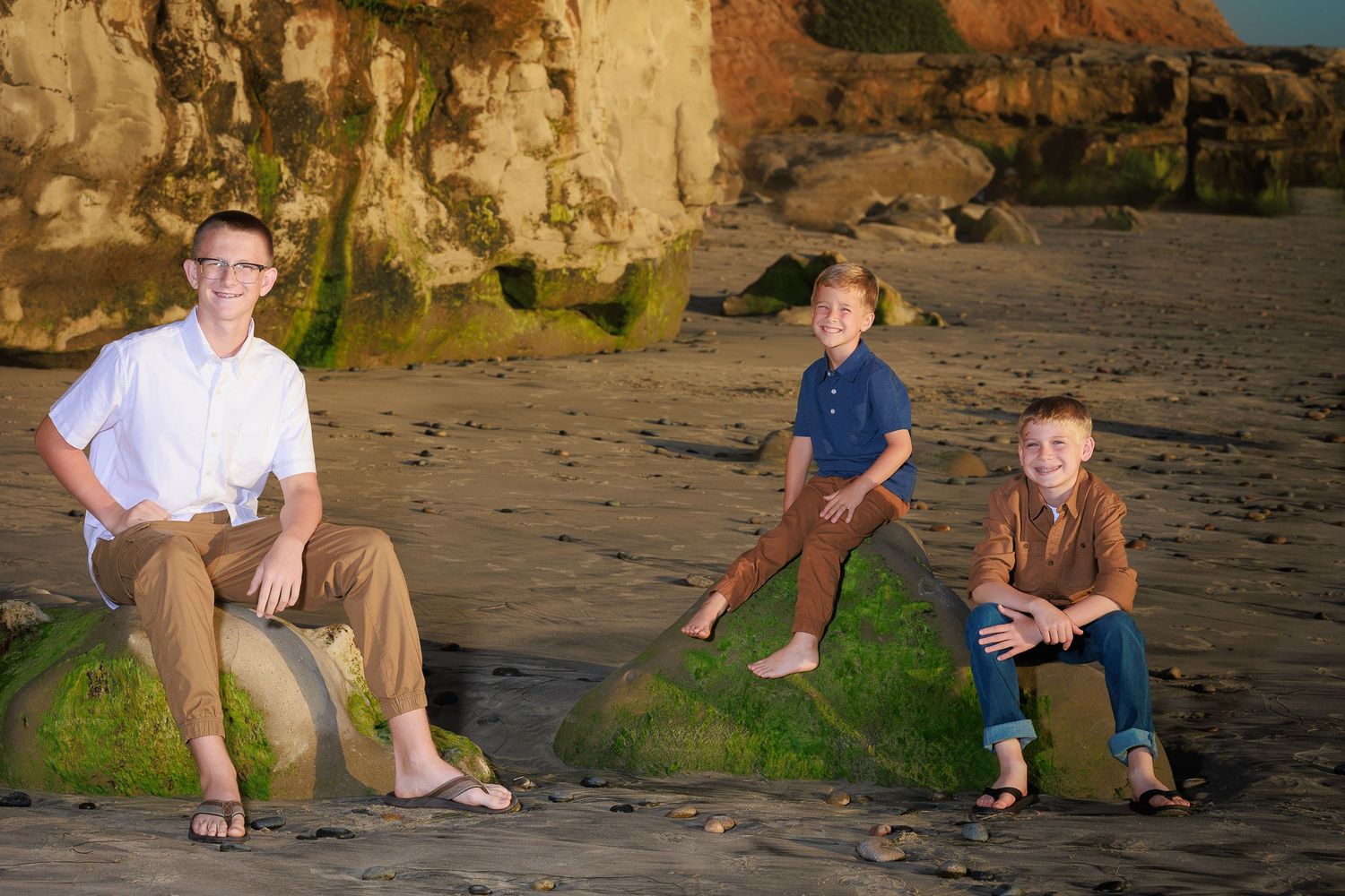 People sitting casually on rocky ledge by the ocean during sunset creating peaceful coastal scene.