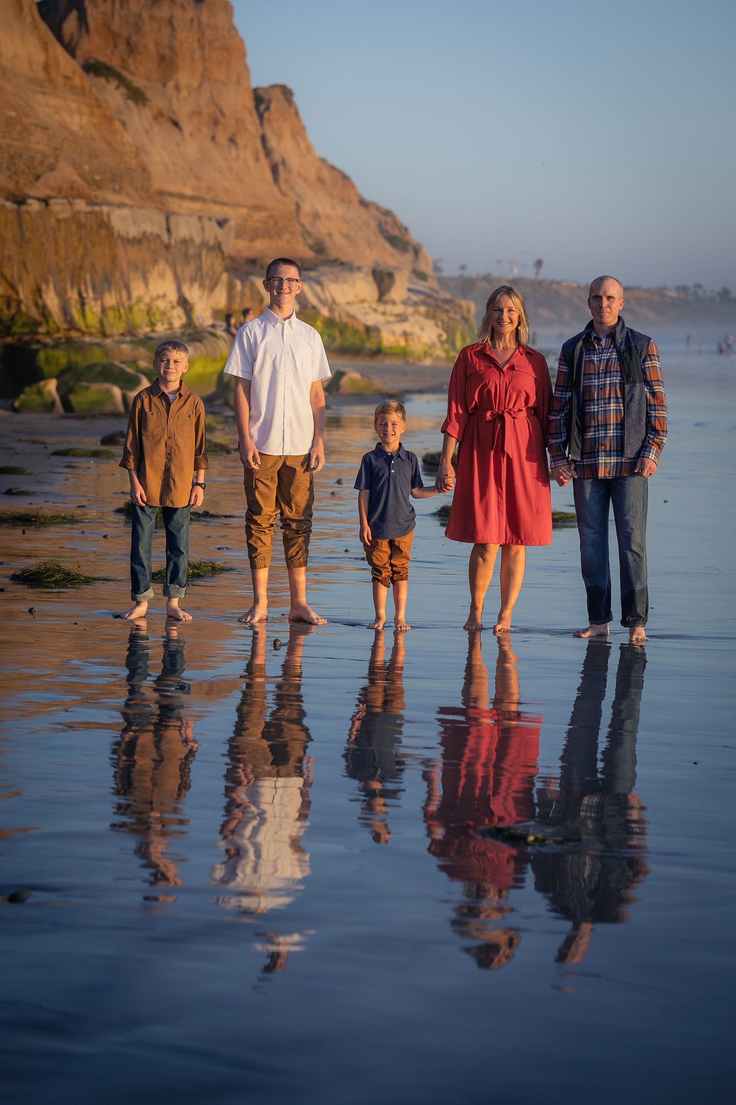 Scenic beach portrait with reflections on wet sand below coastal cliffs at sunset.