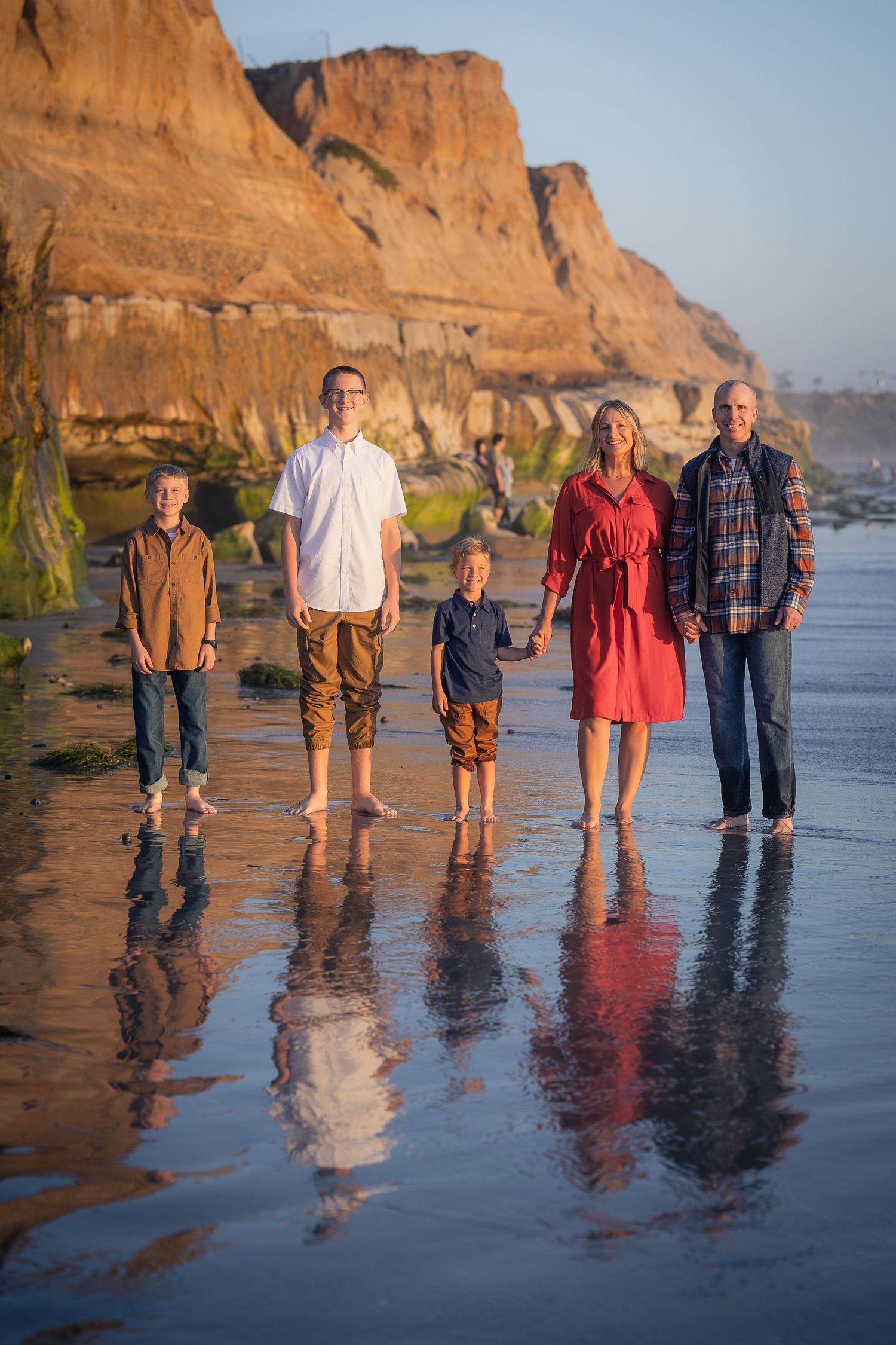 A group of people standing on a wet sandy beach at sunset with tall coastal cliffs in the background.