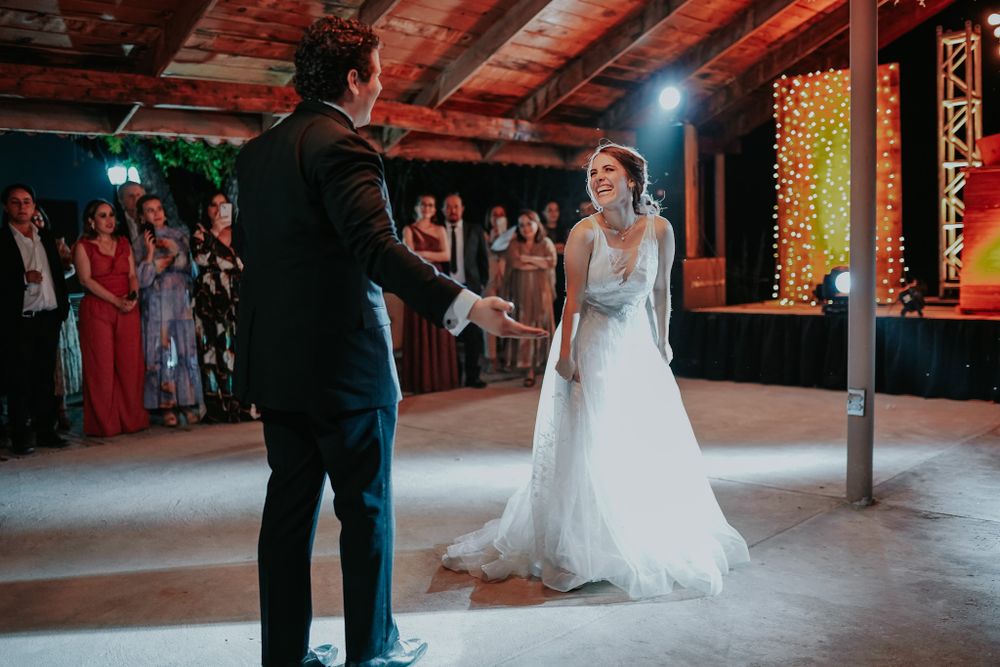 A couple shares their first dance in a rustic venue with warm lighting and guests watching.
