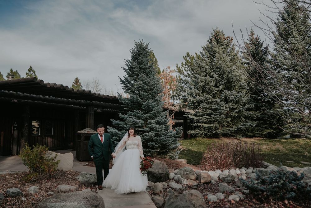 Wedding couple walking path through evergreen trees in winter landscape.