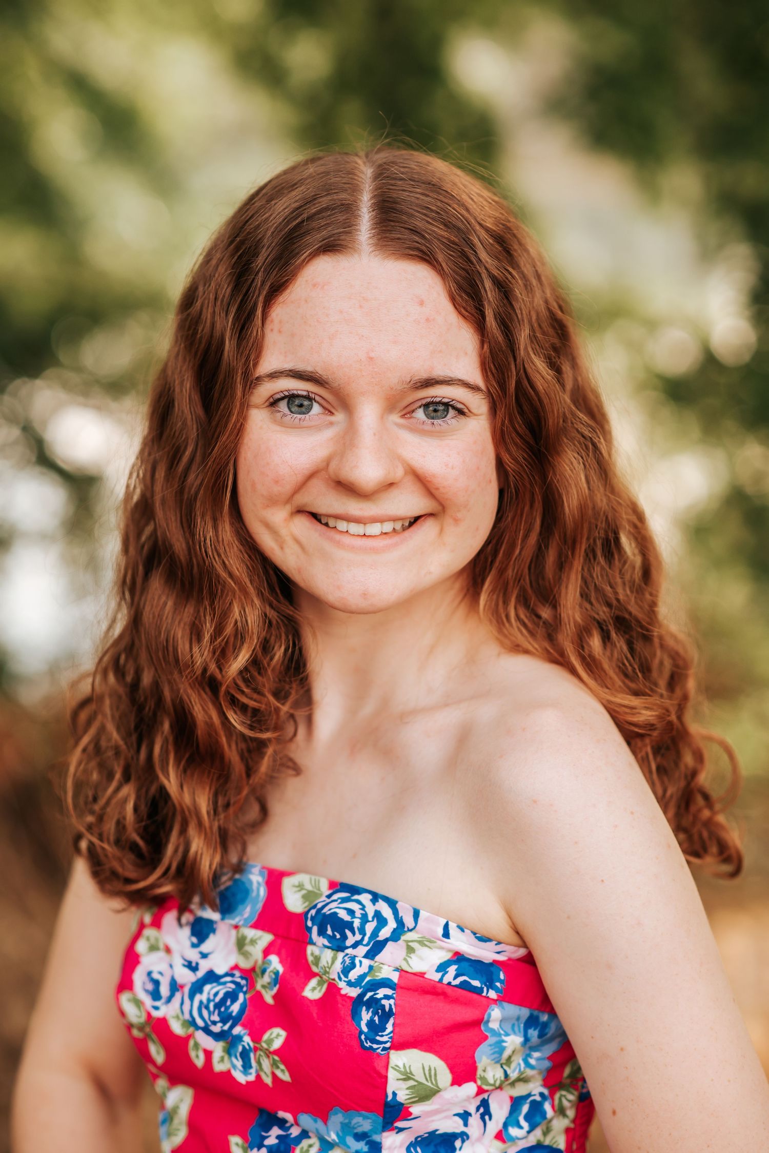 High school senior wearing floral print dress smiling brightly in senior photo session in Tri Cities, Washington.