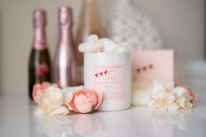 Pink champagne bottles and floral scented candle alongside delicate roses and petals on white surface.