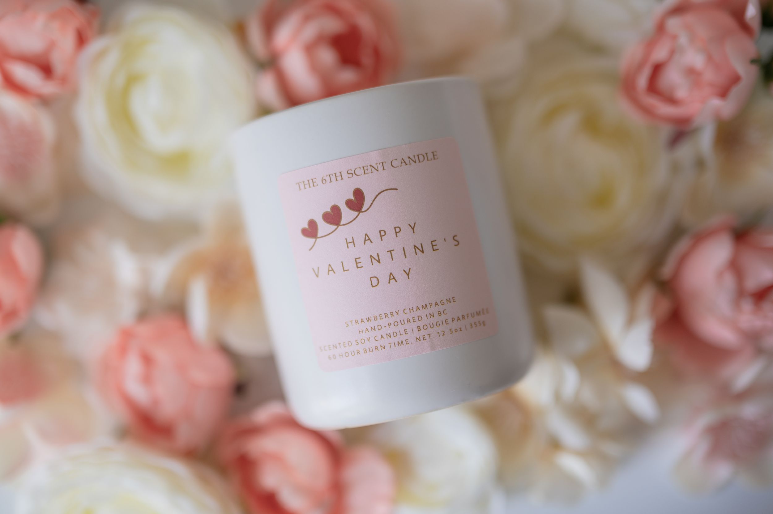 White candle with pink label against backdrop of soft pink and white roses.