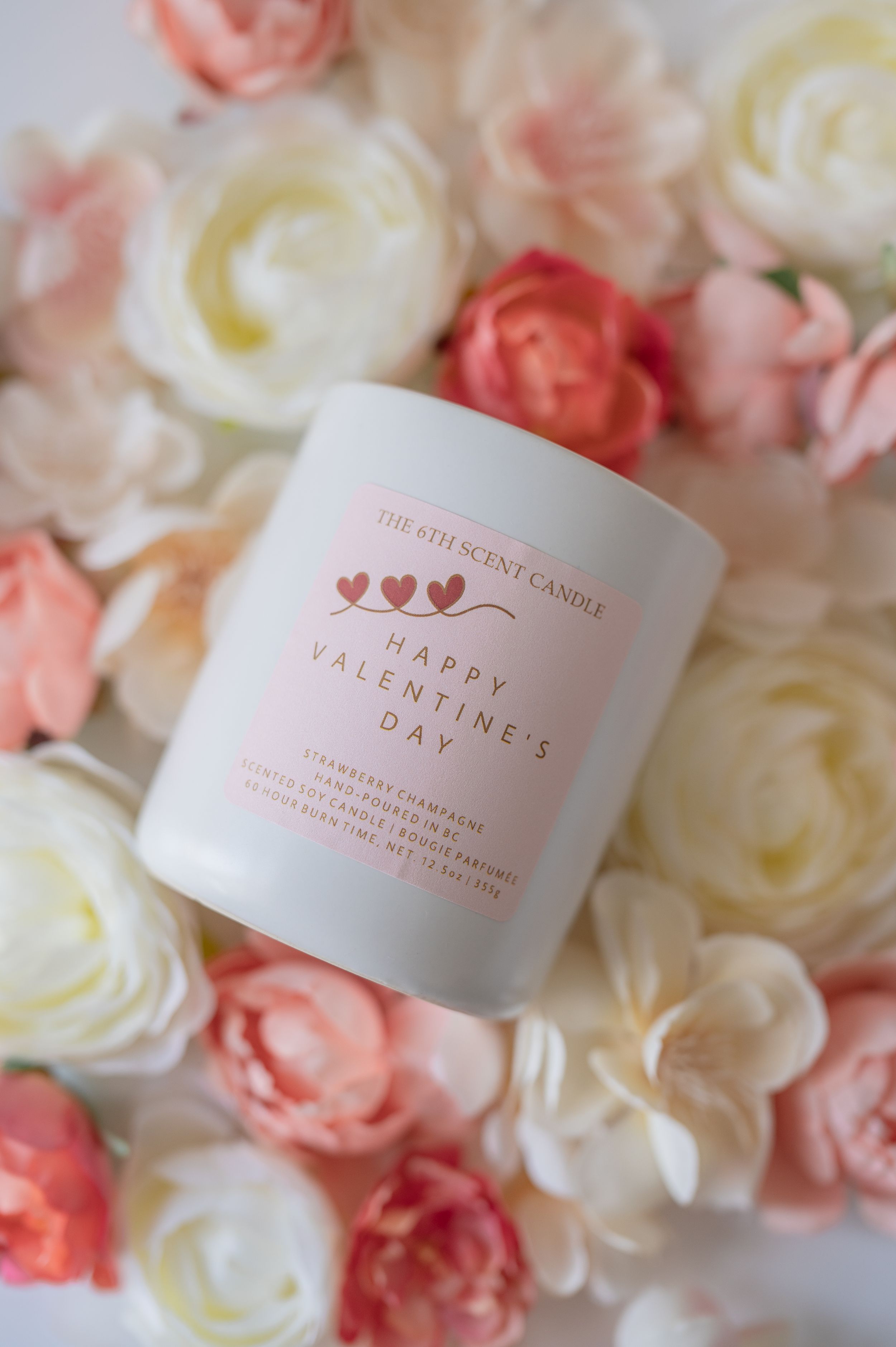 Pink Valentines Day candle surrounded by delicate coral and white roses on a soft floral background.