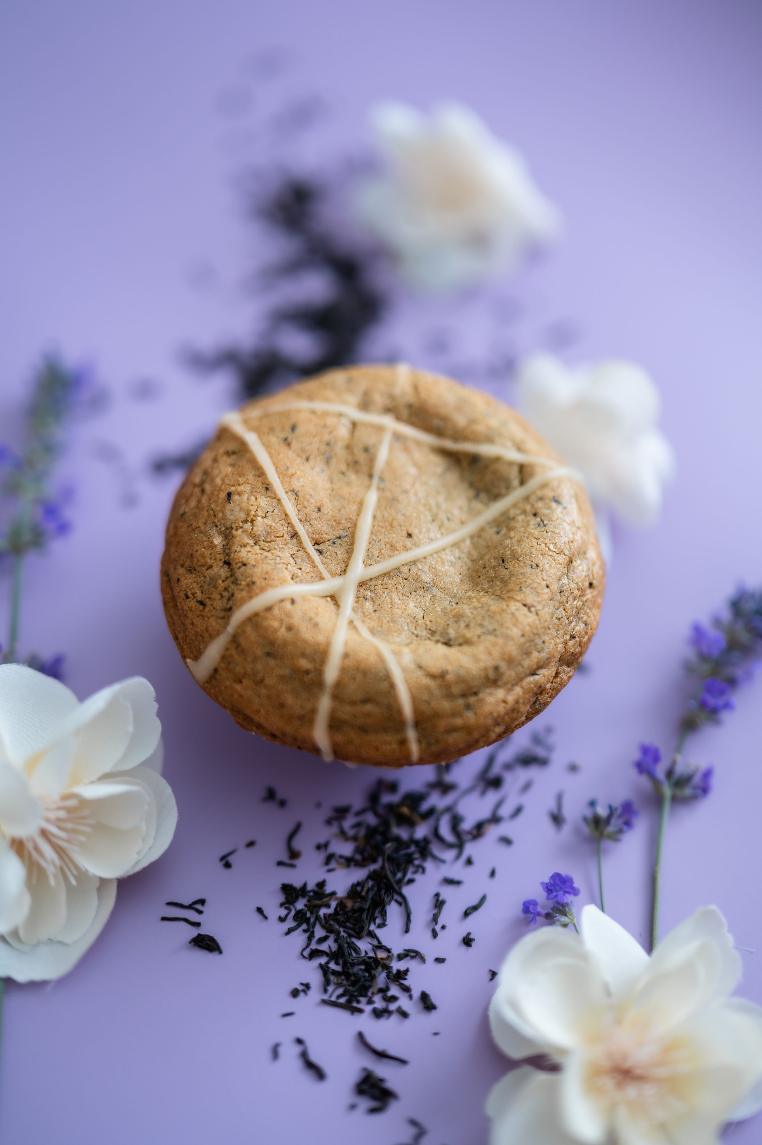 A round shortbread cookie decorated with white icing lines on purple background with lavender sprigs and white flowers.