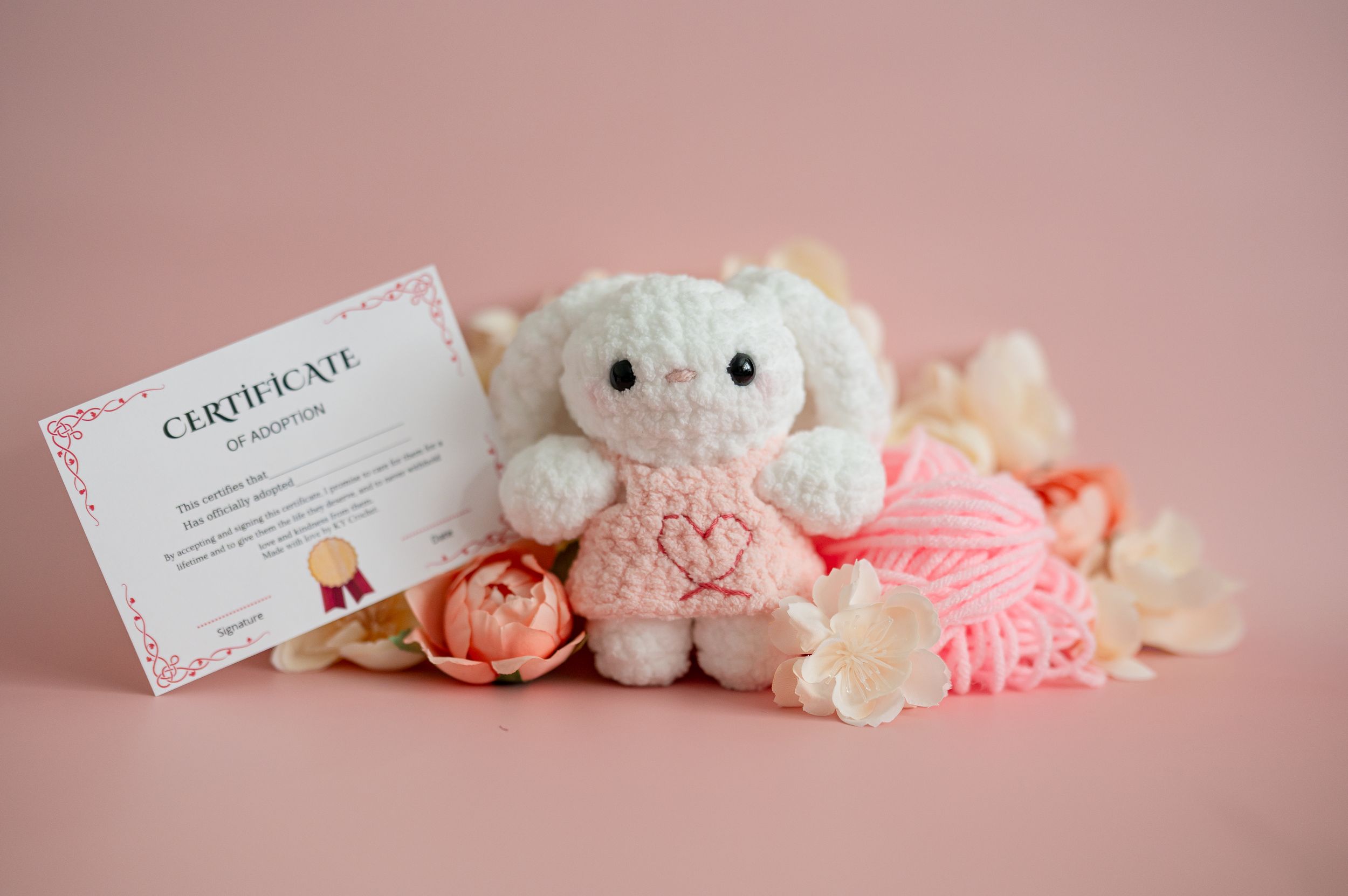 A soft pink gift certificate lies beside delicate flowers and a plush teddy bear on a blush-colored background.
