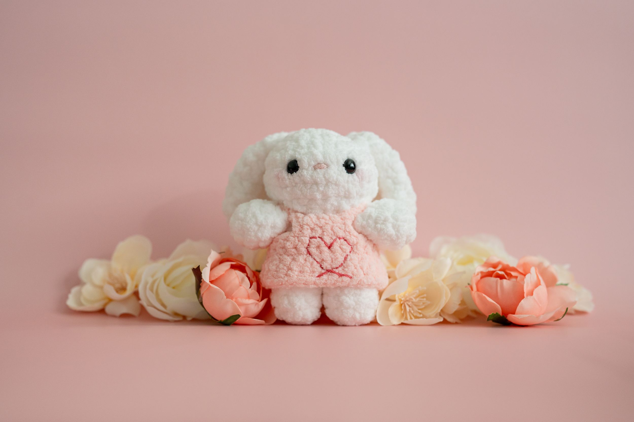 Soft pink and cream colored plush toys arranged in a row against a pastel pink background.