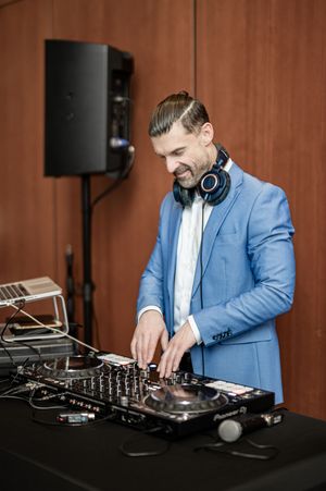 DJ in a blue blazer and white shirt performs at an event using professional mixing equipment.