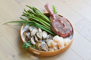 Fresh seafood platter with scallops, oysters and asparagus beside a cut of meat.