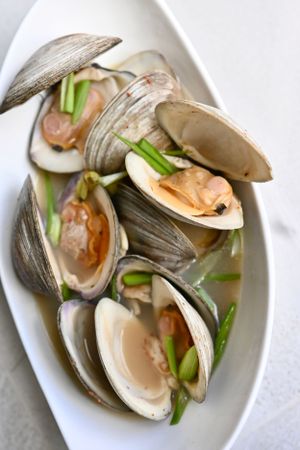 Steamed clams garnished with green onions served on white oval plate.