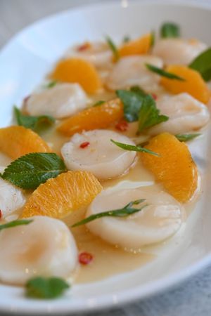 Scallop crudo garnished with orange segments, herbs and red pepper flakes.