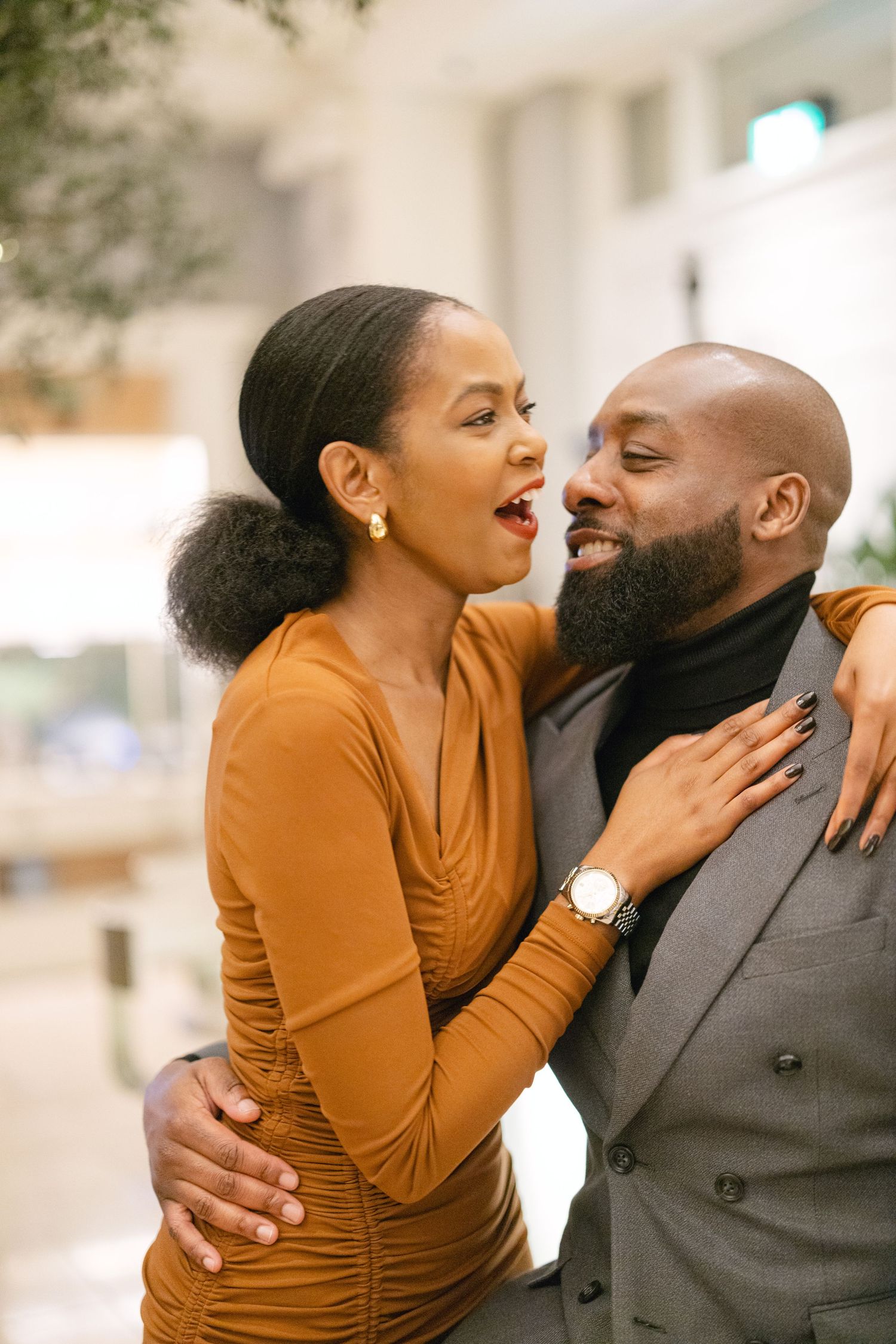 A joyful couple embraces while sharing a genuine laugh together in a warmly lit indoor setting.