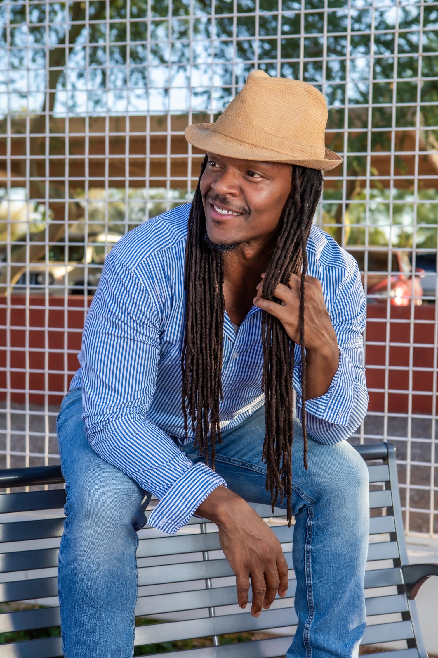 Casual outdoor portrait in striped shirt, jeans and tan hat on park bench.