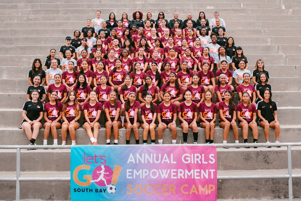 Large group photo at Annual Girls Empowerment Soccer Camp on stadium steps with Let's Go South Bay banner.