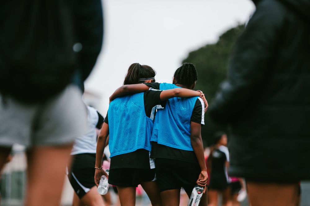 Two female athletes in blue vests walk arm in arm after a race.