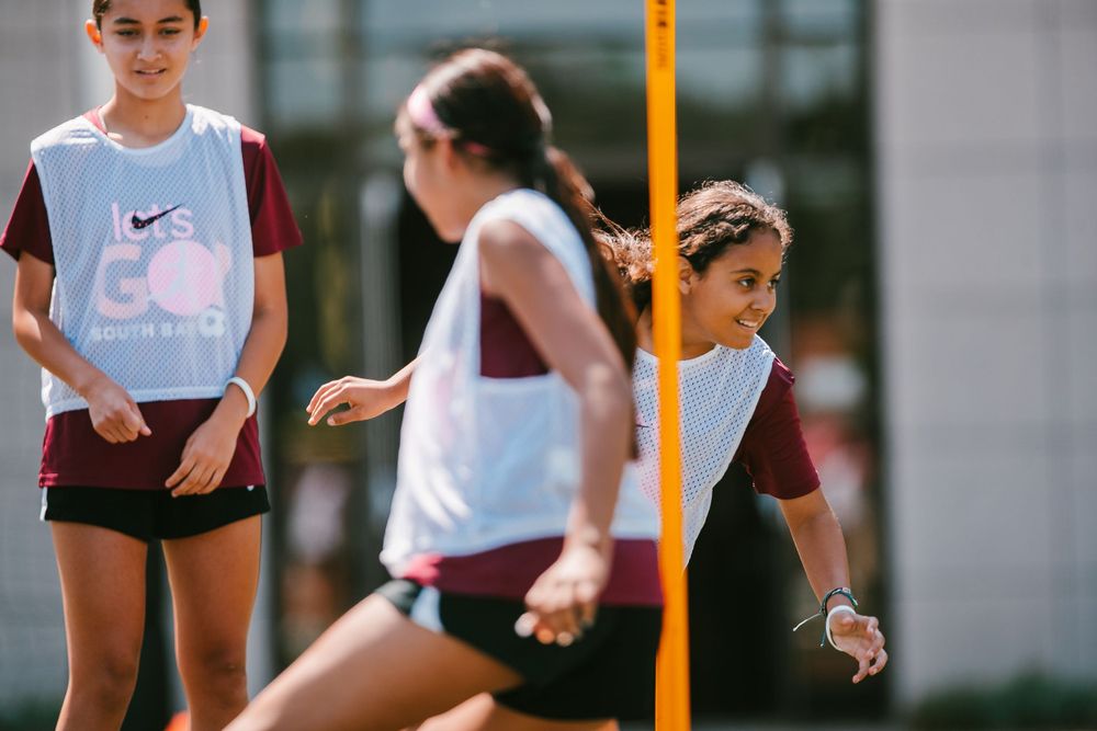 Young female athletes practice soccer drills around orange poles during outdoor training session.