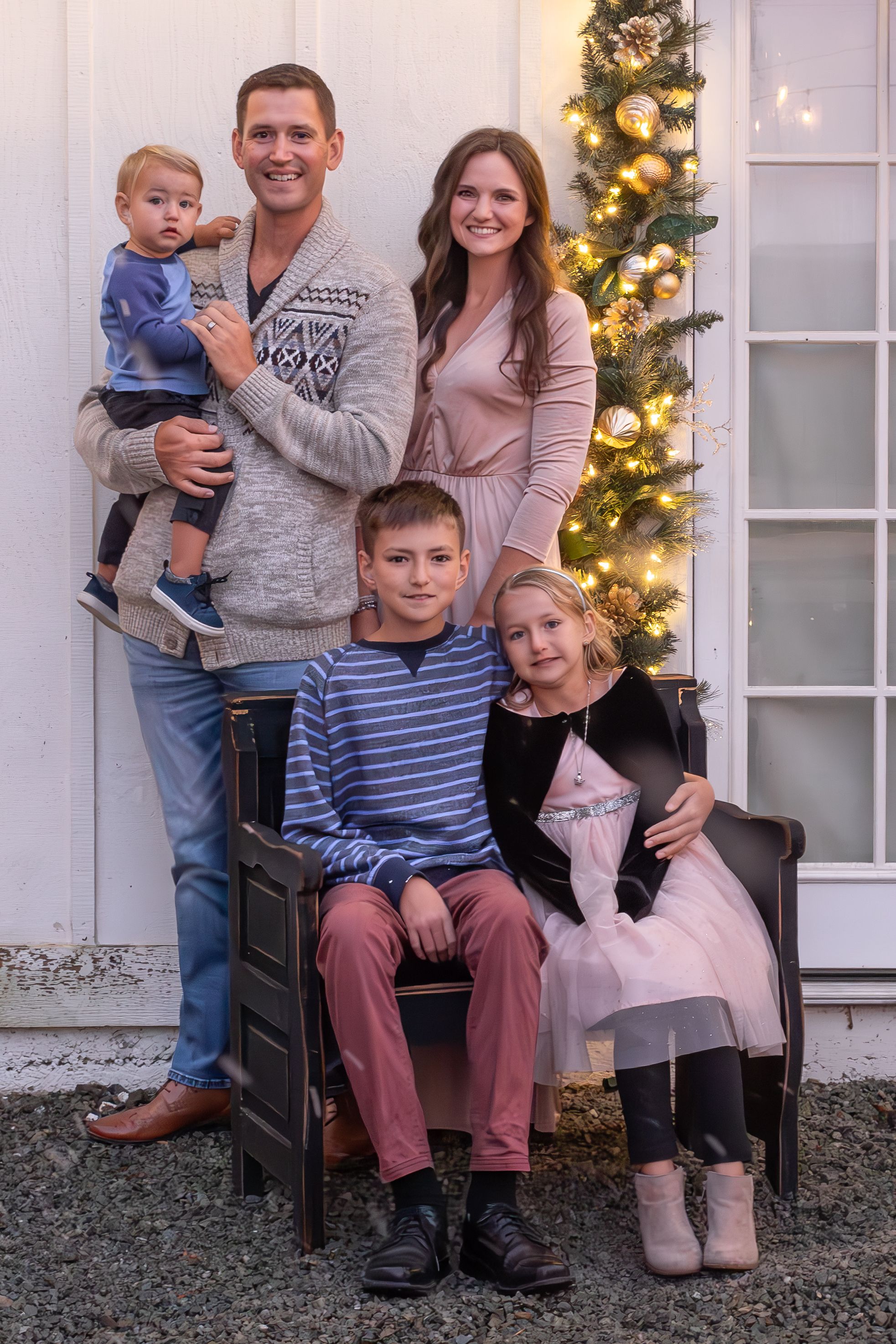 Family of five poses for holiday portrait in front of decorated Christmas tree with twinkling lights.
