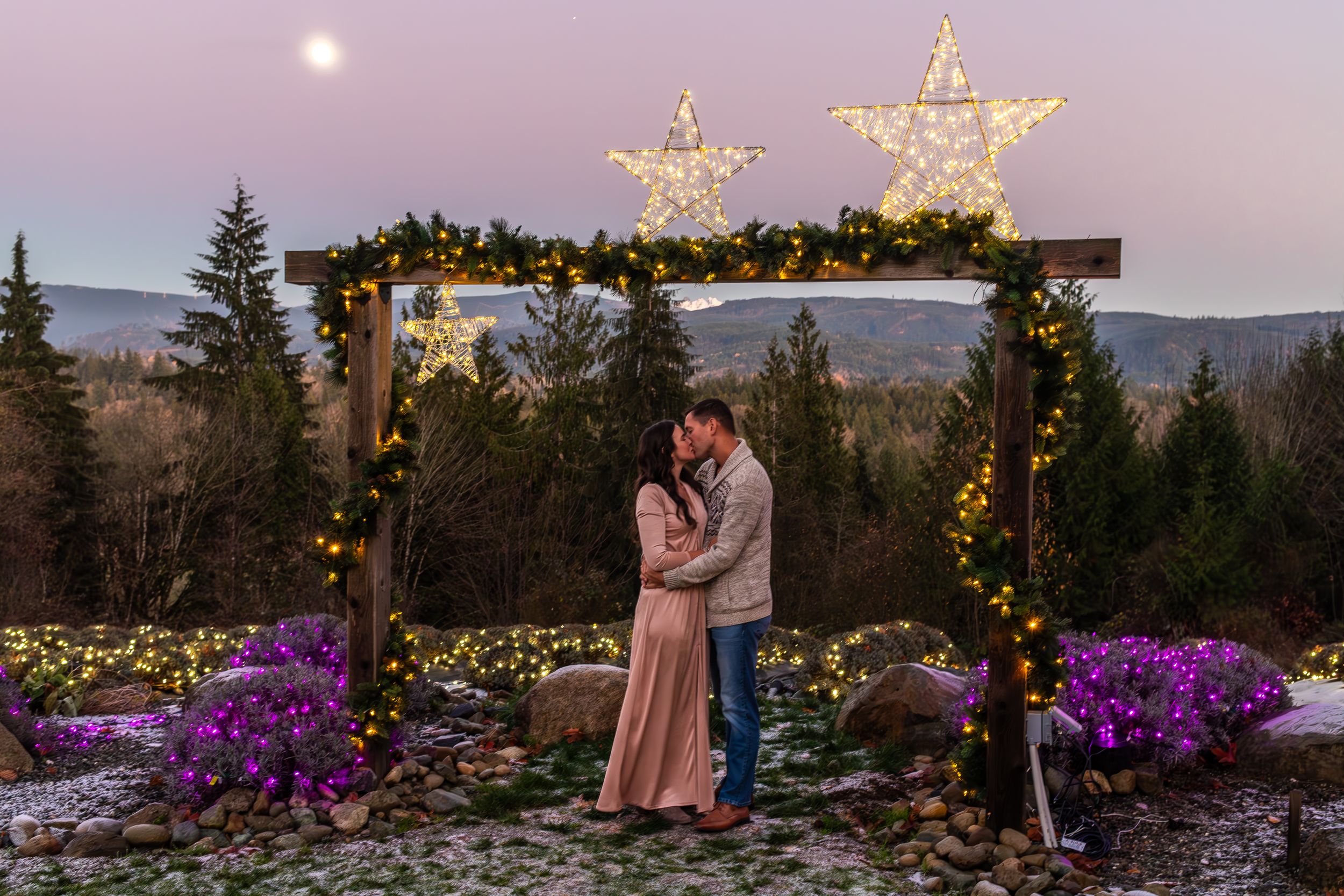 Couple embracing under lit archway with star decorations at twilight.