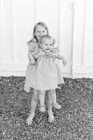 Black and white portrait of two young children in matching light-colored dresses.