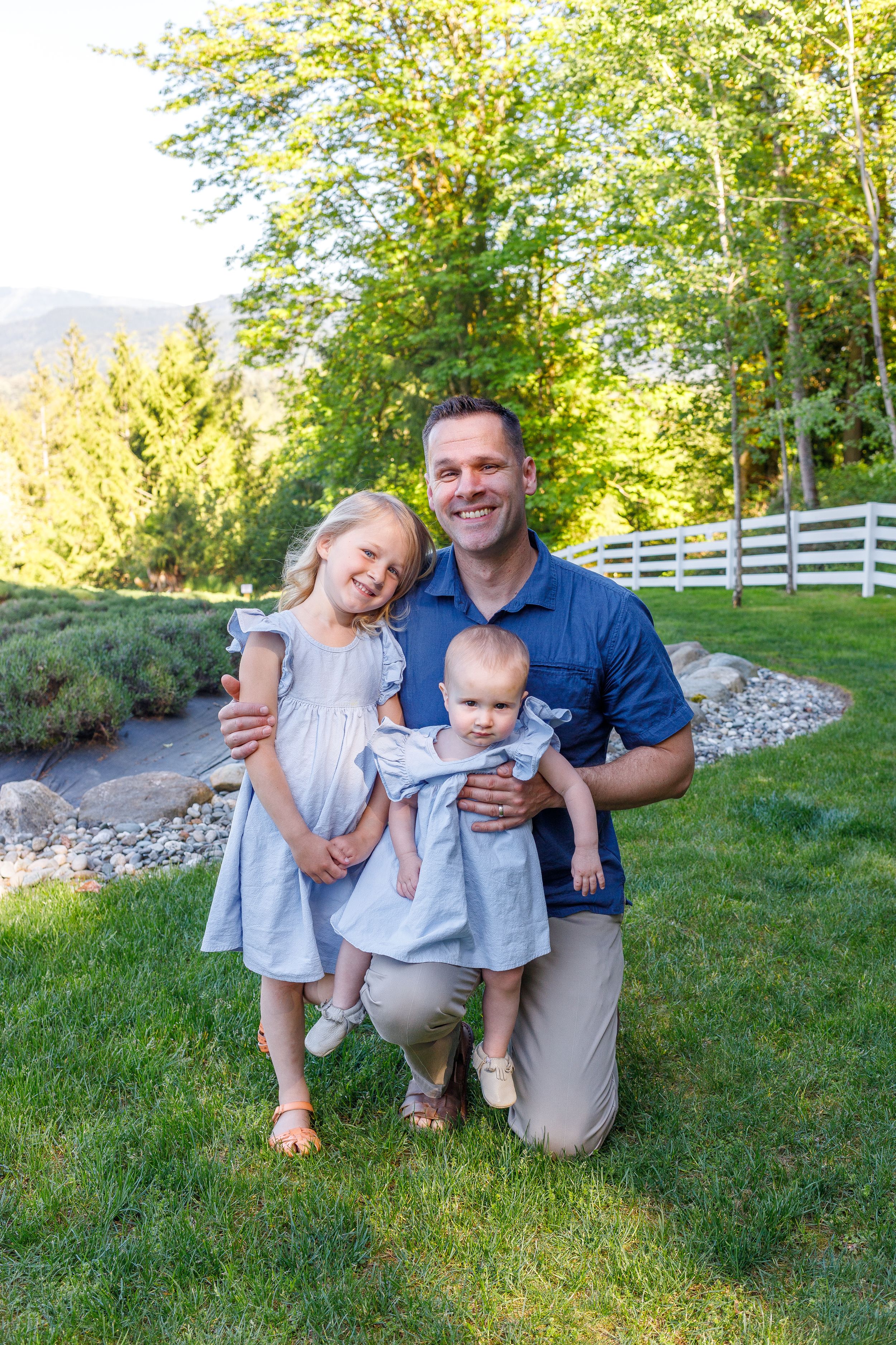 Family portrait on green lawn with white fence and mountains in background.